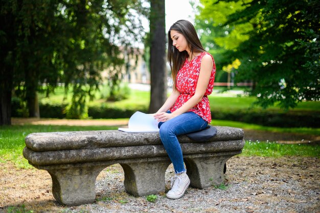 Hermosa estudiante universitaria leyendo un libro en un banco en un parque