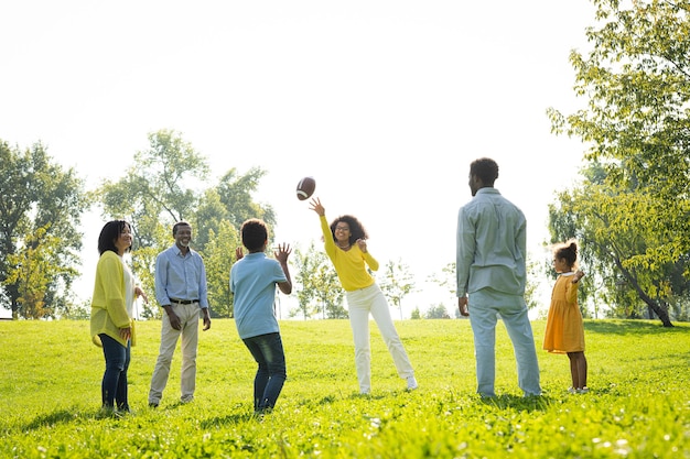 Hermosa familia afroamericana feliz que se une en el parque - Familia negra divirtiéndose al aire libre, padres e hijos jugando al fútbol