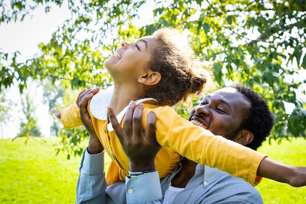 Hermosa familia afroamericana feliz uniéndose en el parque - Familia negra divirtiéndose al aire libre, papá jugando con su linda hija