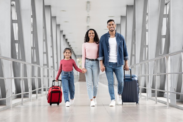 Hermosa familia árabe de tres con maletas caminando juntas en la terminal del aeropuerto