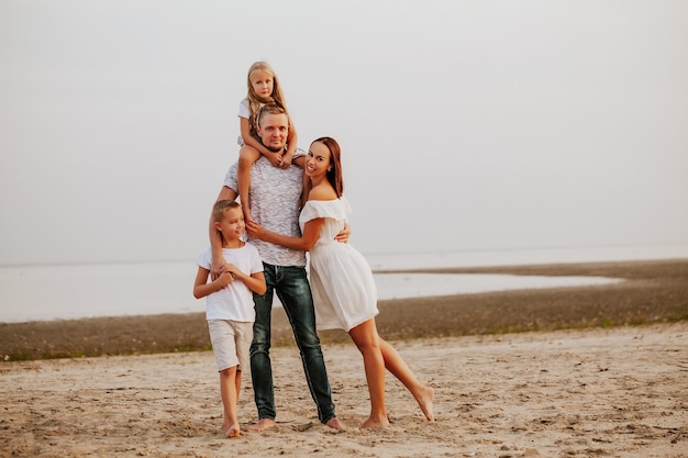 Foto una hermosa familia con dos hijos en ropa de colores claros posan y sonríen en la orilla arenosa