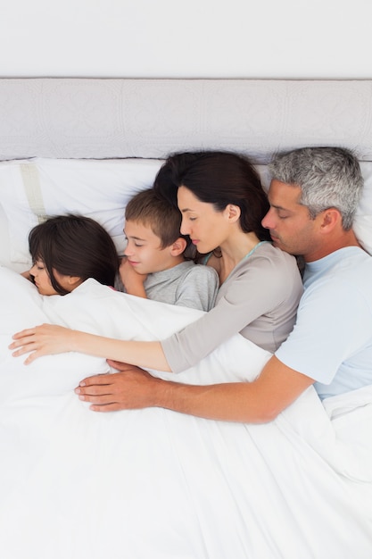 Hermosa familia durmiendo juntos en la cama en casa