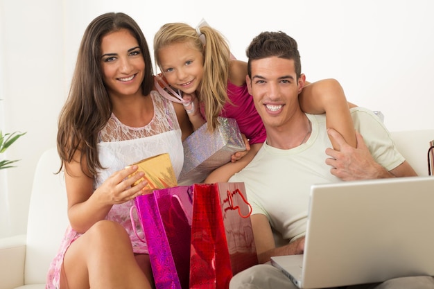 Hermosa familia feliz sentada en casa con laptop y bolsas de compras.