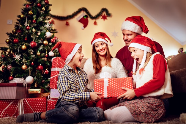 Hermosa familia feliz con sombrero de santa y se sorprenden con regalos de Navidad en casa.