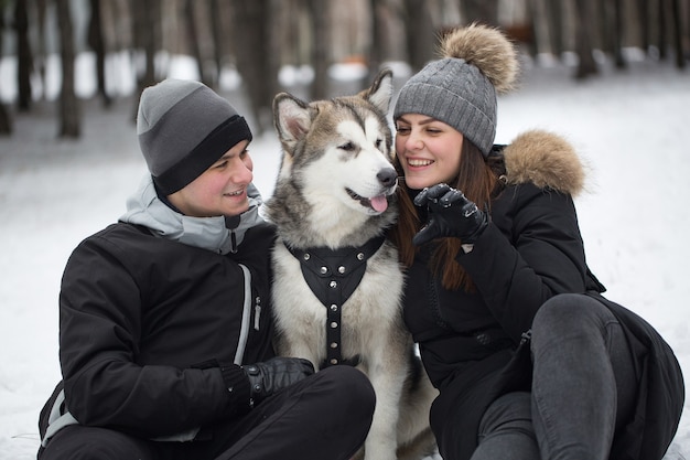 Hermosa familia, un hombre y una niña en el bosque de invierno con perro. Juega con el perro husky siberiano.