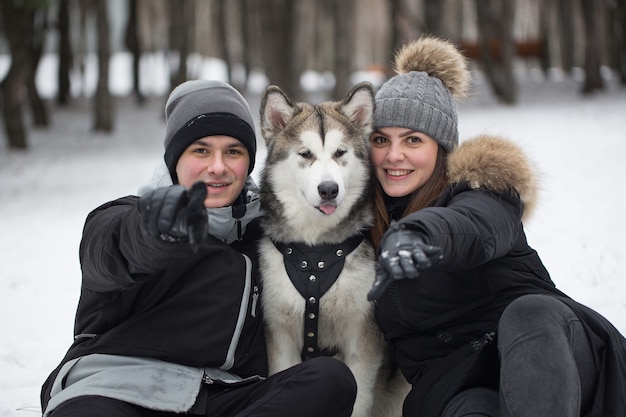 Hermosa familia, un hombre y una niña en el bosque de invierno con perro. Juega con el perro husky siberiano.