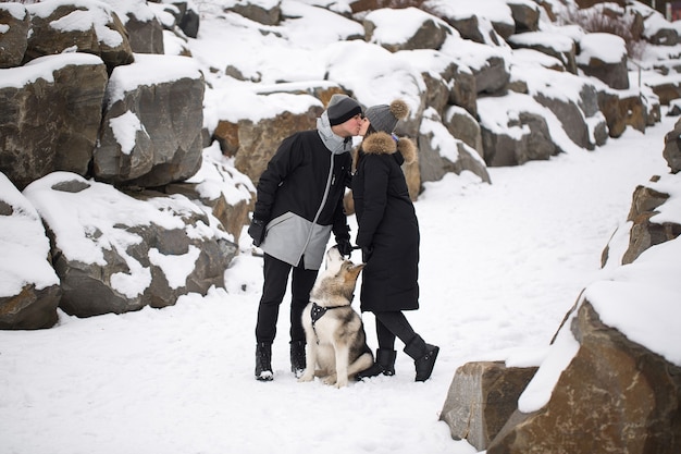 Hermosa familia, un hombre y una niña en el bosque de invierno con perro. Juega con el perro husky siberiano.