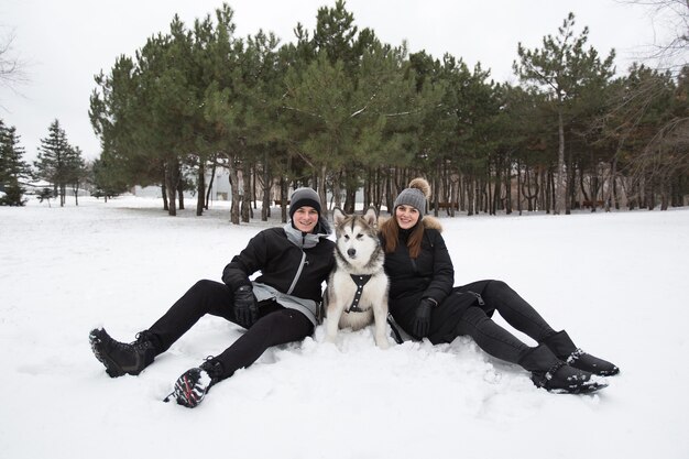 Hermosa familia, un hombre y una niña en el bosque de invierno con perro. Juega con el perro husky siberiano.