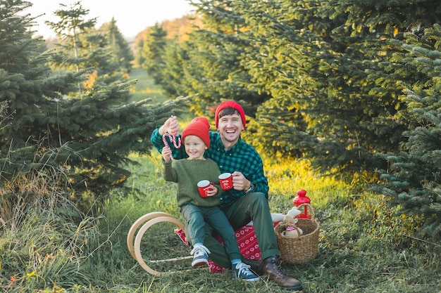 Una hermosa familia joven elige un árbol de Navidad en el mercado Vacaciones de invierno festivas para padres y niños pequeños Ecológico Beber té en la naturaleza