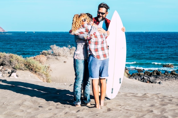 Hermosa familia junta para siempre en la playa con un día soleado y un adolescente surfista - hablando juntos con una mesa de surf y gente feliz - vacaciones de verano - vista trasera