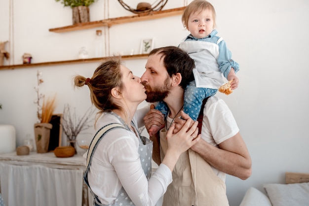 Hermosa familia de mamá, papá y bebé está preparando masa y abrazándose en la cocina