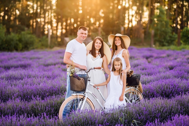 Hermosa familia mamá papá y sus hijas en un campo de lavanda con una bicicleta. Fotos de verano bajo los rayos del sol vespertino.