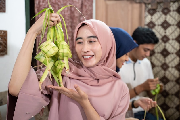 Hermosa familia musulmana y amigo haciendo pastel de arroz ketupat en casa usando hojas de palma para la tradición de eid fitr mubarak