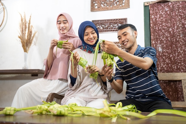 Hermosa familia musulmana y amigo haciendo pastel de arroz ketupat en casa usando hojas de palma para la tradición de eid fitr mubarak