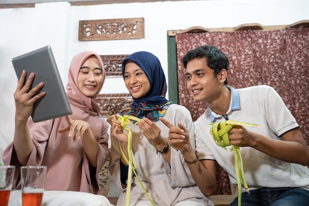 Hermosa familia musulmana y amigo haciendo pastel de arroz ketupat en casa usando hojas de palma para la tradición de eid fitr mubarak