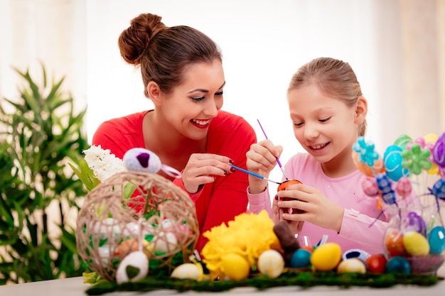 Hermosa felicidad madre e hija pintando huevos de Pascua en casa.