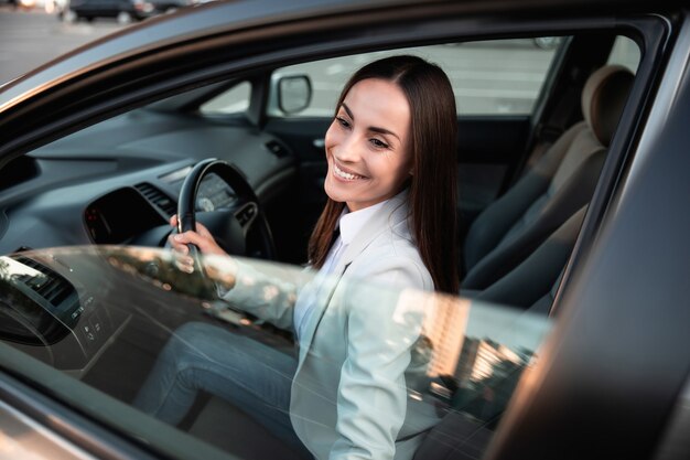 Hermosa feliz empresaria exitosa está conduciendo un automóvil nuevo y moderno de buen humor. Retrato femenino lindo conductor coche de dirección con cinturón de seguridad