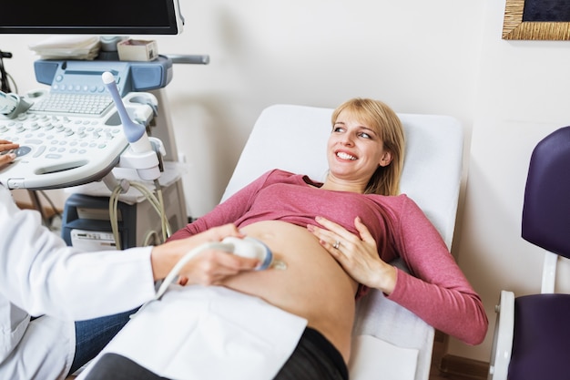 Hermosa y feliz futura madre haciendo ecografía en la clínica prenatal.