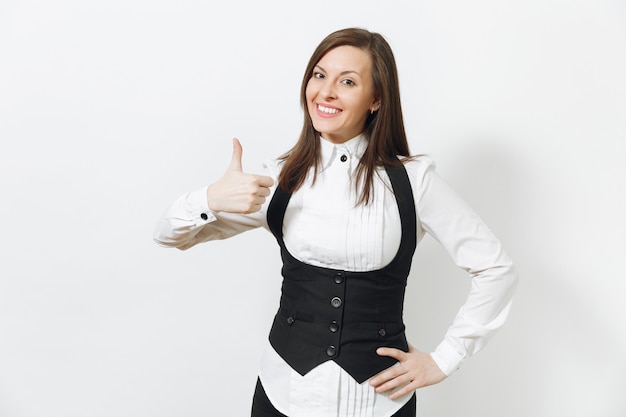 Hermosa feliz joven caucásica sonriente mujer de negocios de cabello castaño en traje negro, camisa blanca y gafas mostrando el pulgar hacia arriba aislado en la pared blanca