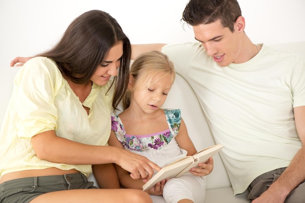 Hermosa feliz joven madre y padre y su linda hija sentada en casa y leyendo un libro