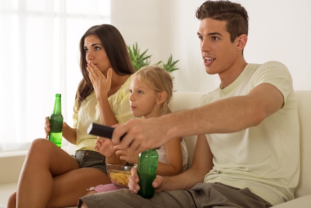 Hermosa feliz joven madre y padre y su linda hija sentada en casa y viendo películas.