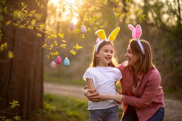 Foto hermosa y feliz madre e hija en orejas de conejo decoran el árbol con huevos de pascua familia feliz celebrando la pascua