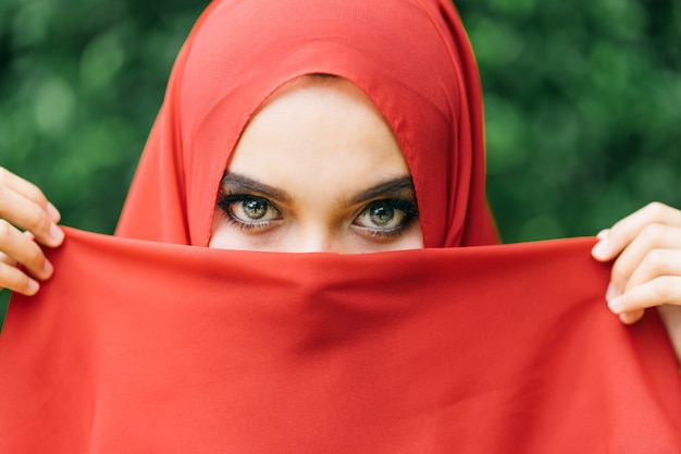 Hermosa de feliz mano de mujer musulmana joven levanta la tela de la cara con el hijab rojo