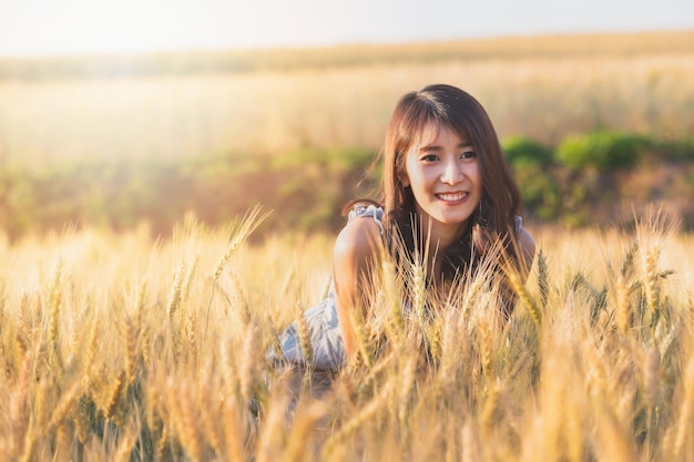 Hermosa y feliz mujer asiática disfrutando de la vida en el campo de cebada al atardecer