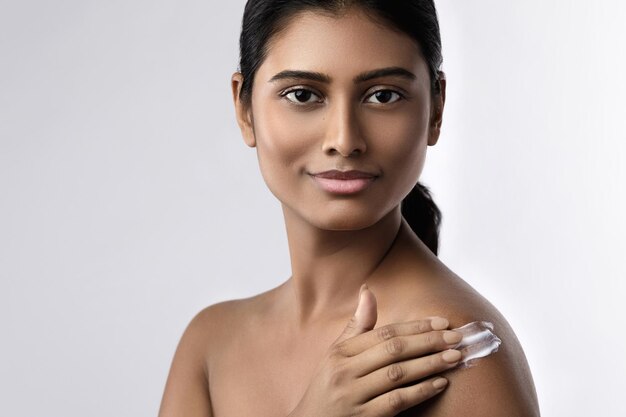 Hermosa y feliz mujer india aplicando crema hidratante o loción bloqueadora solar en su cuerpo