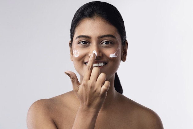 Hermosa y feliz mujer india aplicando crema hidratante en su rostro