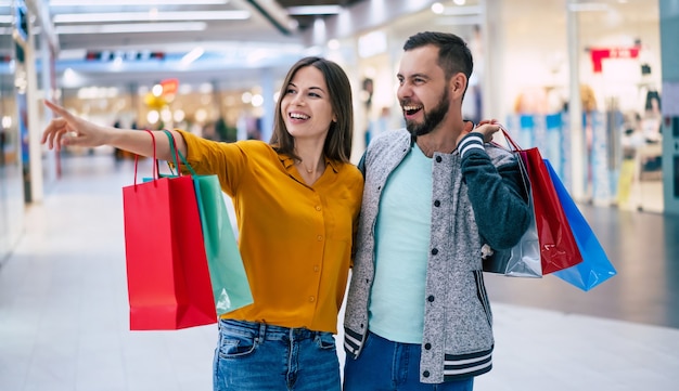 Hermosa feliz pareja emocionada enamorada o familia con bolsas de papel en las manos mientras camina durante las compras en el centro comercial