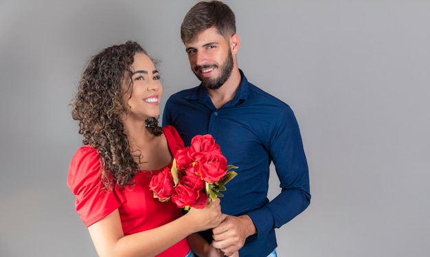 Hermosa feliz pareja positiva abrazándose mirándose sosteniendo un ramo de rosas rojas sobre fondo gris Día de San Valentín