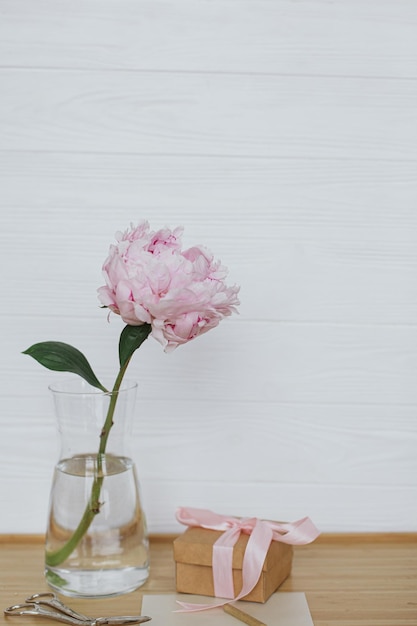 Hermosa flor de peonía en florero caja de regalo tijeras de tarjetas de felicitación en el espacio de copia de fondo de madera