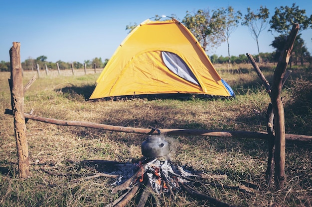 Foto hermosa fogata, madera quemada por carpa en las noches de verano. y la tetera están en primer plano y enfocadas, hay una carpa en el fondo y desenfocada