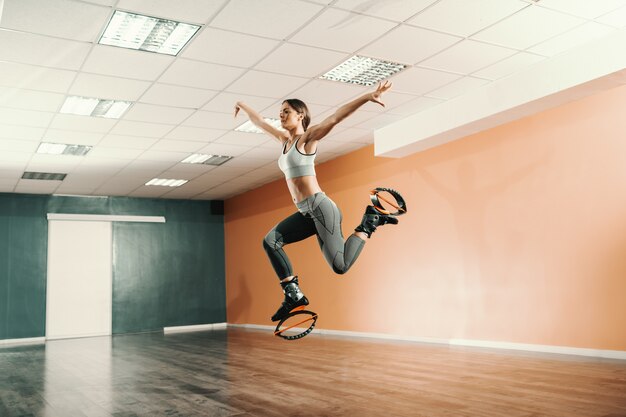 Hermosa forma caucásica morena en ropa deportiva saltando en kangoo salta calzado en el gimnasio.