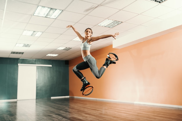 Foto hermosa forma caucásica morena en ropa deportiva saltando en kangoo salta calzado en el gimnasio.