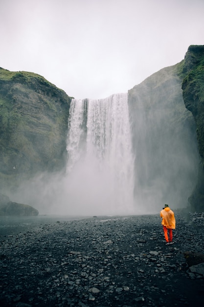 Hermosa foto de una gran cascada con un solo hombre en tela brillante de pie en el área de abajo