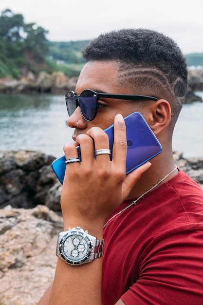 Hermosa foto de un joven con gafas de sol hablando por teléfono con el lago de fondo