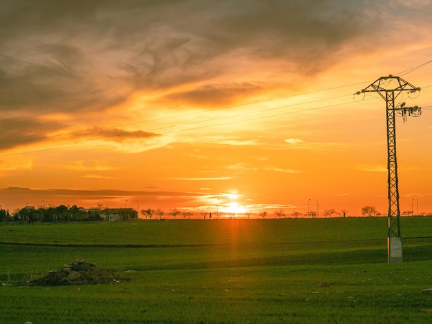 Hermosa foto de una puesta de sol en el campo verde abierto con líneas eléctricas bajo el cielo nublado