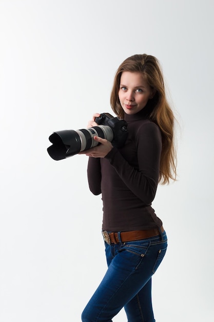 La hermosa fotógrafa con cámara dslr profesional posando sobre un fondo blanco en el estudio