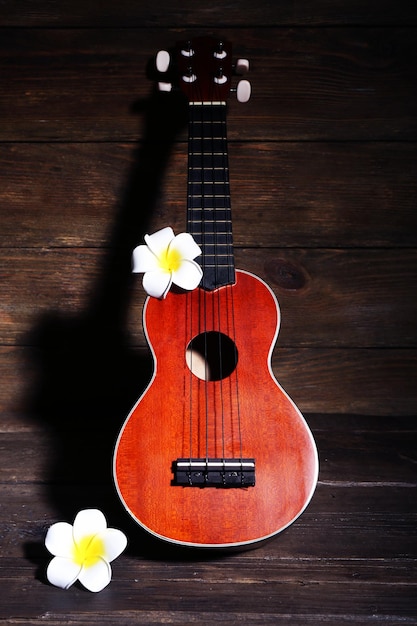 Foto hermosa guitarra acústica hawaiana y flores sobre fondo de madera oscura