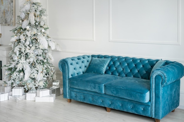 Hermosa habitación decorada de vacaciones con árbol de Navidad, chimenea y sofá Escena de invierno acogedor. Interior blanco con luces. Foto de alta calidad