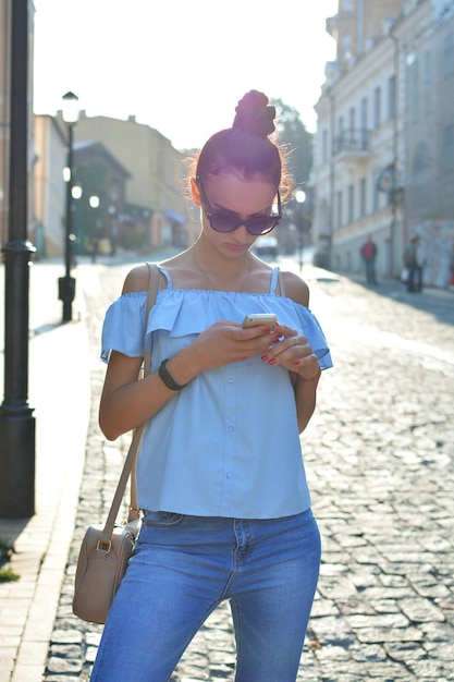 Una hermosa y hermosa mujer joven con cabello oscuro está leyendo un mensaje en el teléfono contra un fondo de calle de la ciudad