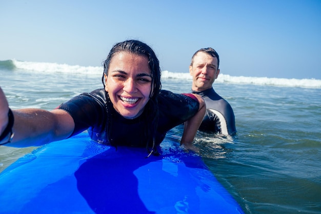 Hermosa instructora de surf latinoamericana haciendo foto selfie con un amigo en un teléfono inteligente con cámara en vacaciones de verano en el mar indio de Goa