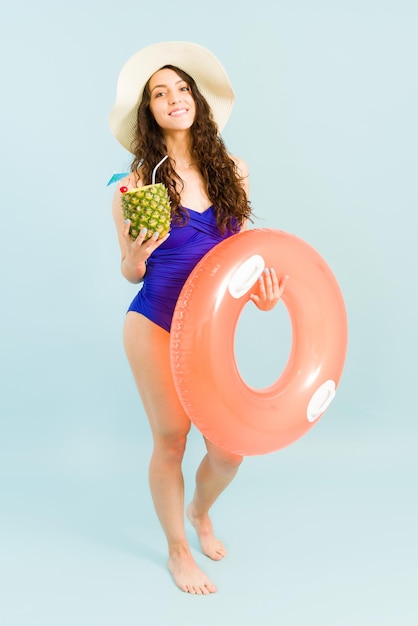 Hermosa joven de unos 20 años sonriendo en la playa. Mujer feliz disfrutando de un cóctel de piña colada mientras lleva un salvavidas inflable