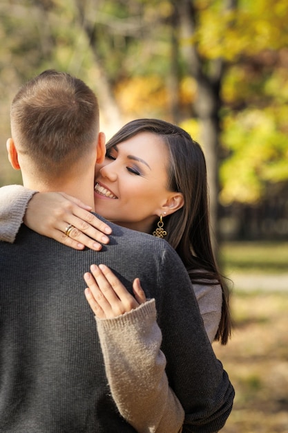 Hermosa joven abrazando amorosamente a su hombre en el parque de otoño vertical