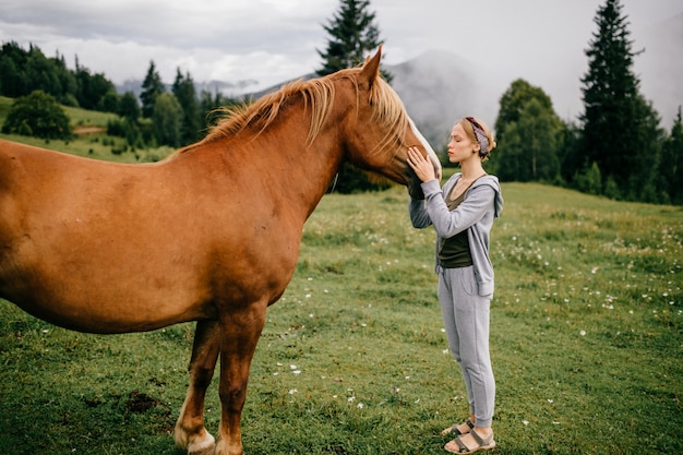 Hermosa joven abrazando a caballo en la naturaleza