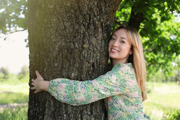 Hermosa joven abrazando el tronco de un árbol en el bosque