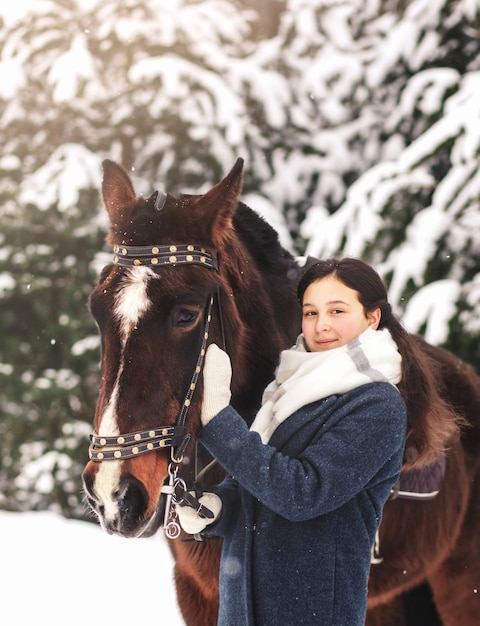 Hermosa joven acaricia un caballo marrón en invierno en la naturaleza