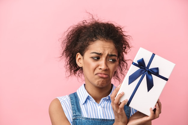 Hermosa joven africana decepcionada con caja de regalo sobre rosa